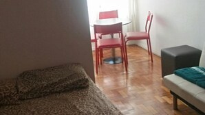A room with a leopard print sofa, a small table with a red chair, and a bench with a teal cushion. - Studio Maximo (Rio de Janeiro)