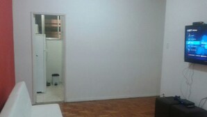 A room with a white couch, a wooden floor, a television mounted on the wall, and a door leading to another room. - Studio Maximo (Rio de Janeiro)