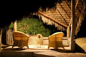 An outdoor seating area with wicker chairs and a table, under a thatched roof structure. - Chalés Recantos do Mar (Cajueiro da Praia)