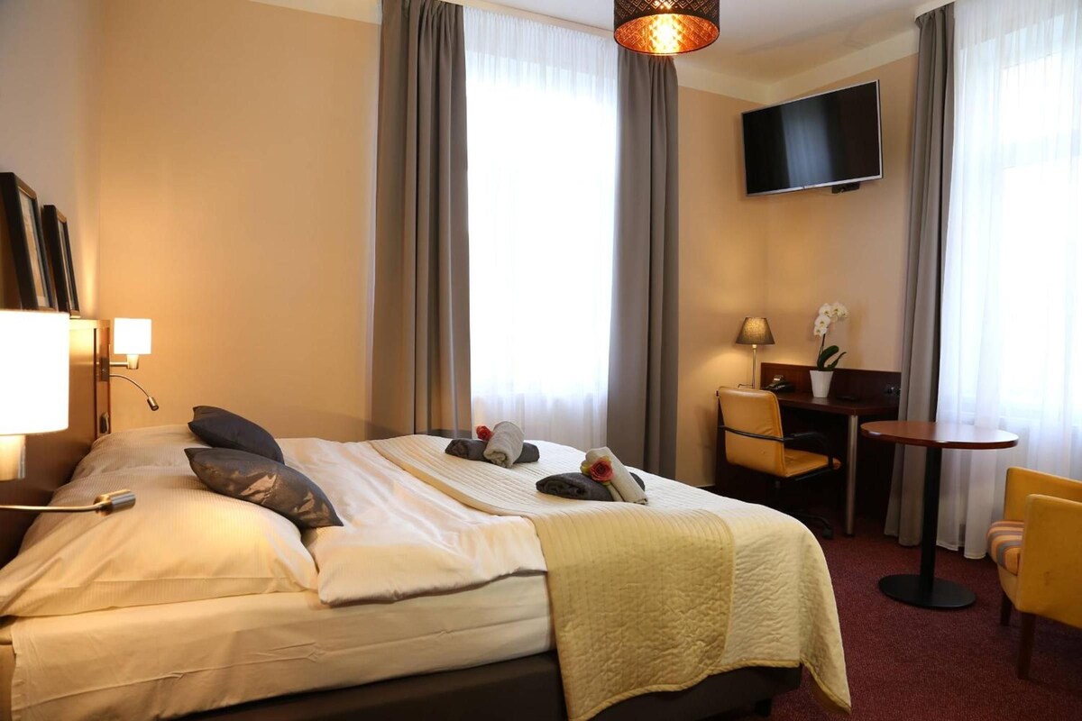 A hotel room with a bed, a desk, a chair, a TV, and a lamp.