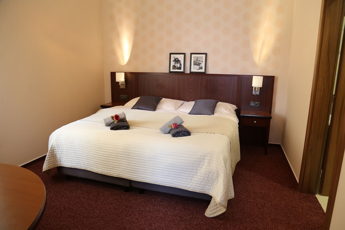 Una habitación de hotel con una cama grande, dos mesitas de noche y una pequeña mesa.