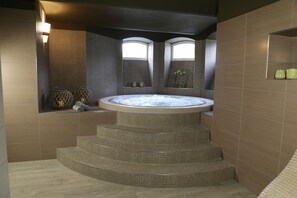 A spa area with a hot tub, steps leading to it, and two windows providing natural light.