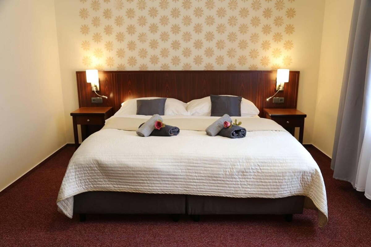 A hotel room with a large bed, two bedside tables, and a floral wallpaper pattern.
