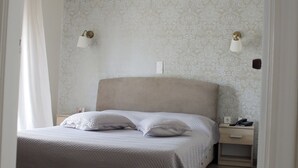 A neatly made bed with a headboard, two bedside lamps, and a nightstand with a phone and a lamp. - Hotel Anesi (Metamorfosi)