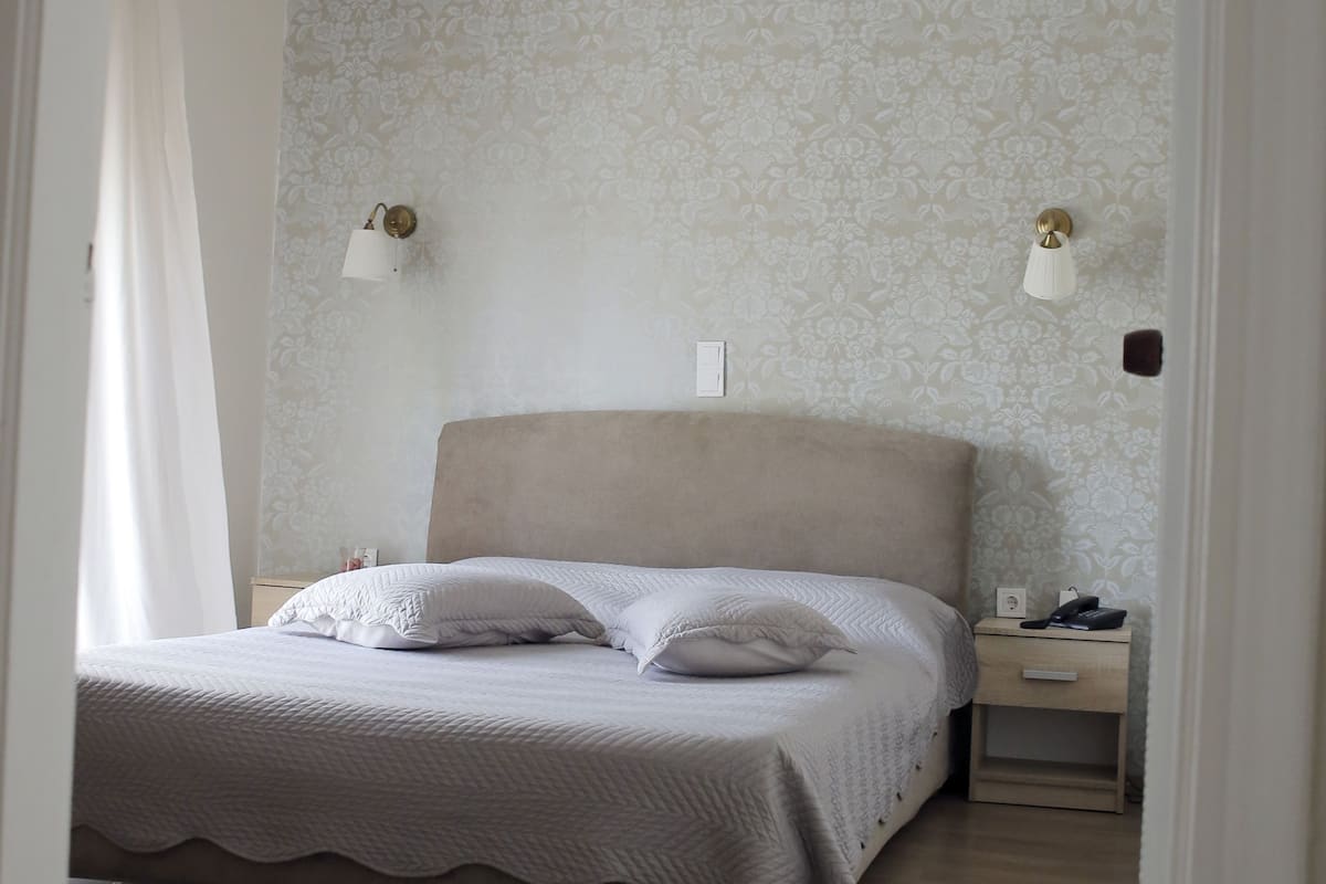 A neatly made bed with a headboard, two bedside lamps, and a nightstand with a phone and a lamp.