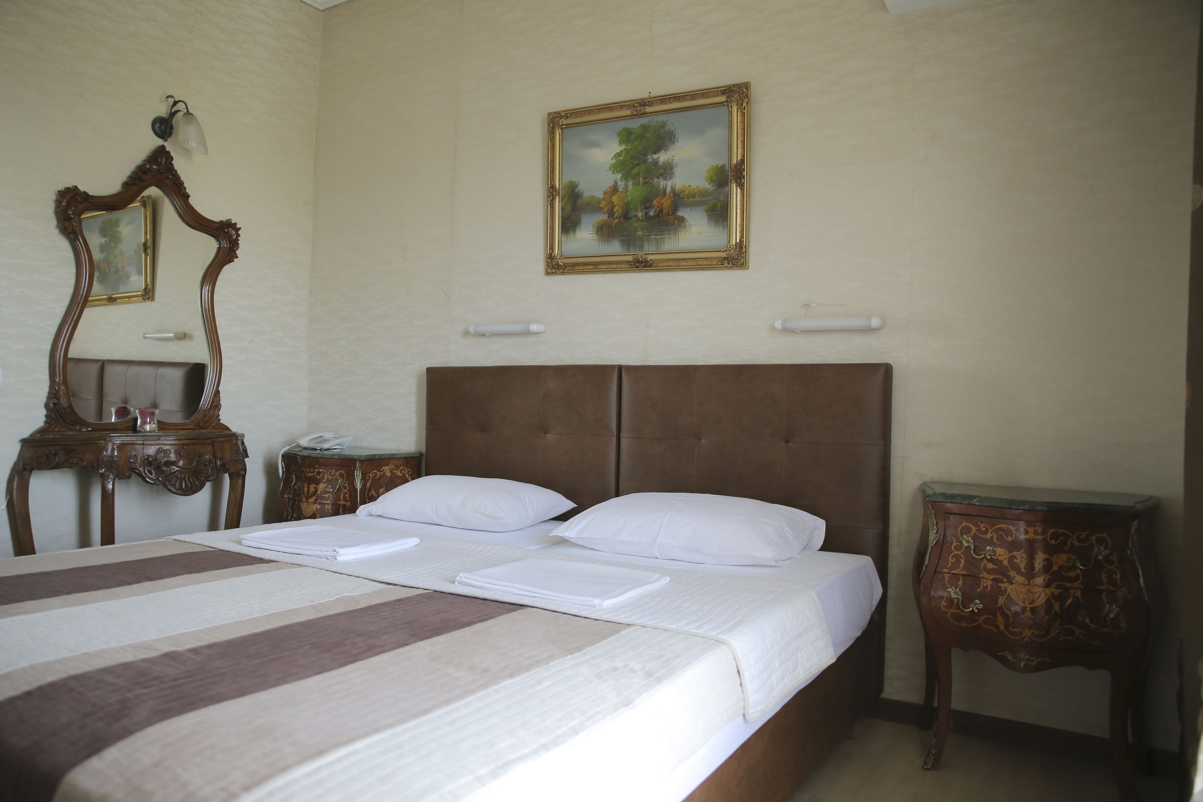 Habitación de hotel con cama doble, cabecera de madera, mesita de noche y un espejo. En la pared, un cuadro enmarco.