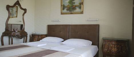 Habitación de hotel con cama doble, cabecera de madera, mesita de noche y un espejo. En la pared, un cuadro enmarco.