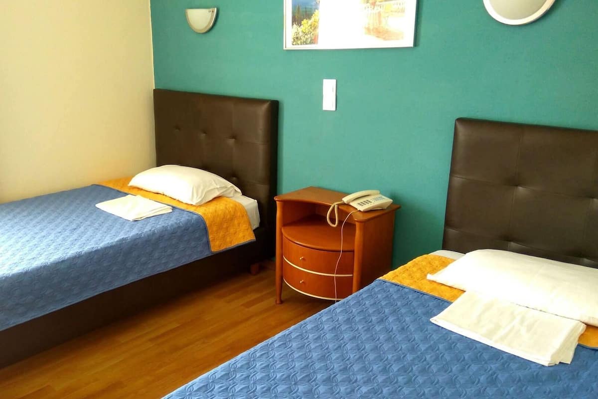 A room with two beds, a wooden nightstand with a phone, and a wall-mounted light fixture.
