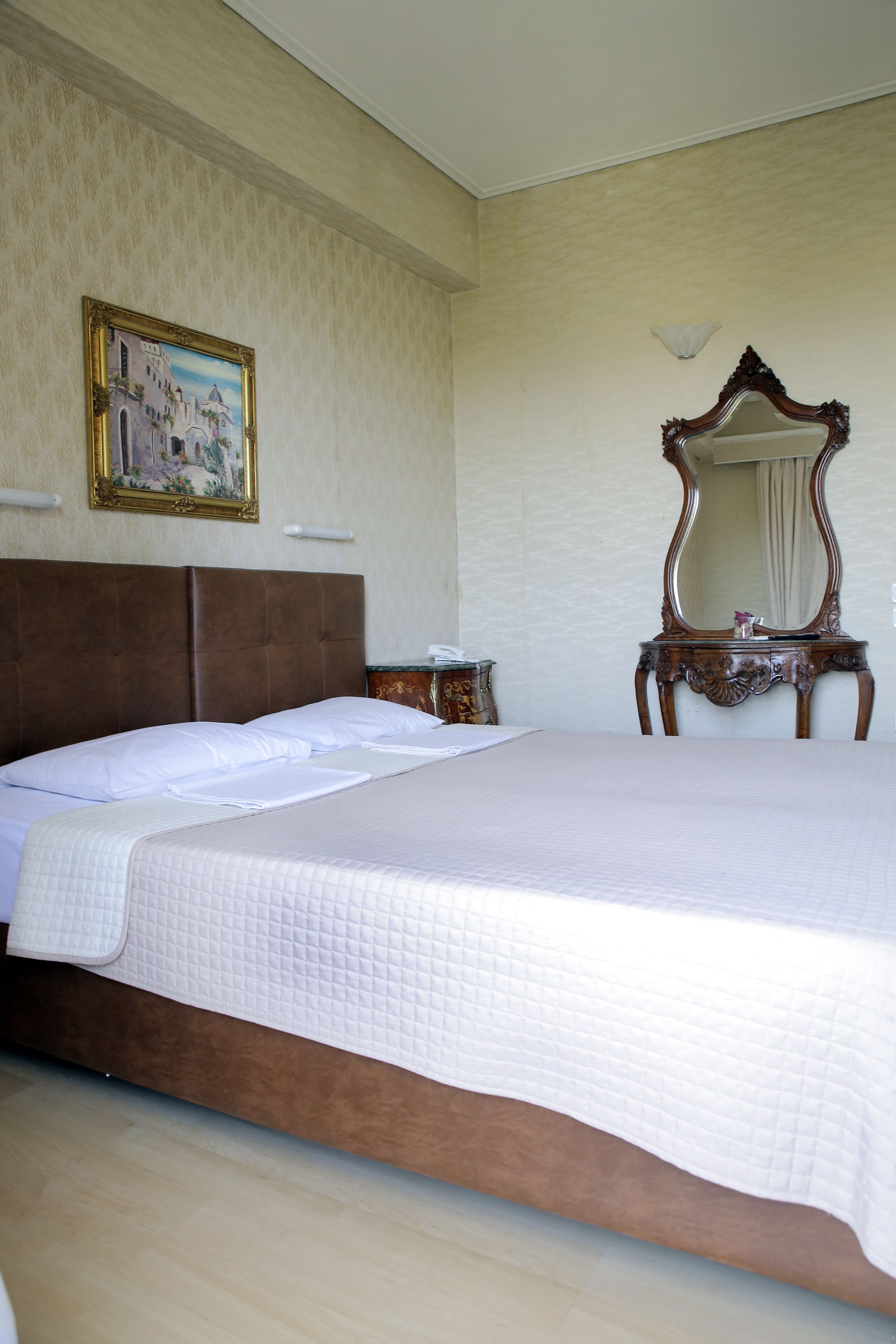 Una cama bien hecha con cabecera, un aparador de madera con espejo y un cuadro en la pared.