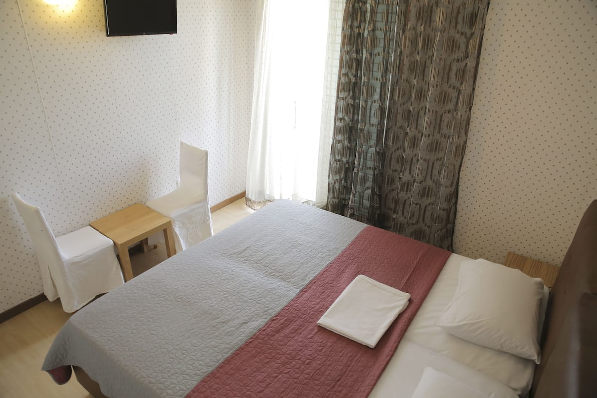 A hotel room with a bed, a desk, a chair, and a TV mounted on the wall.