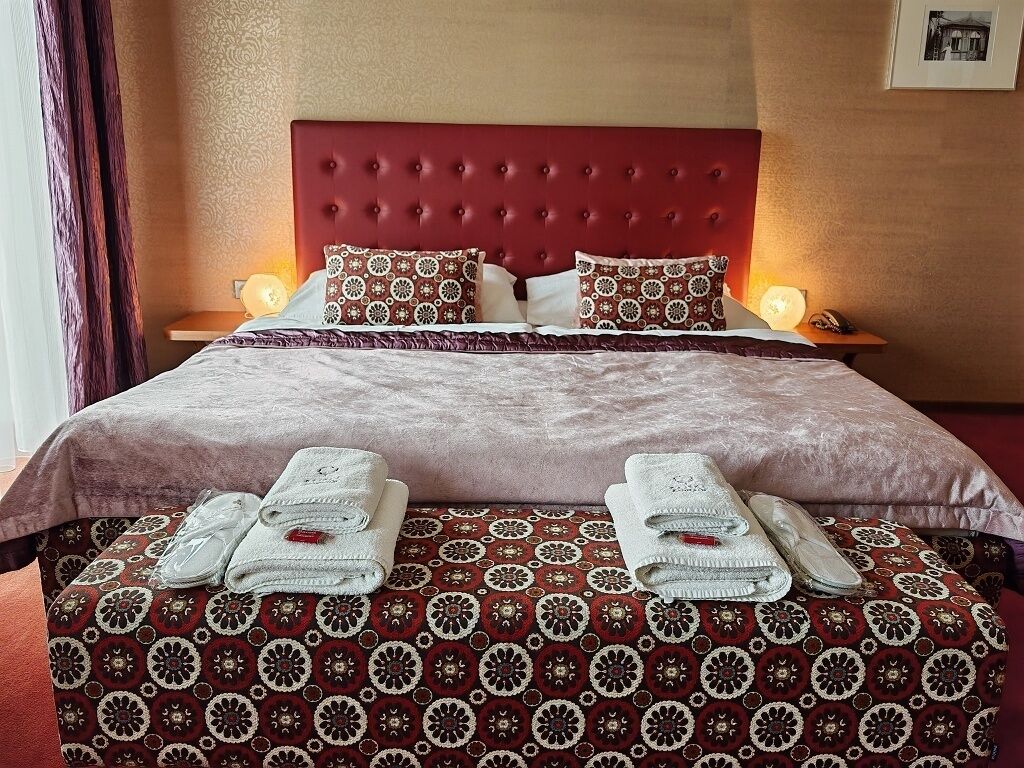 A hotel room with a red headboard, patterned bedspread, and neatly folded towels on the bed.