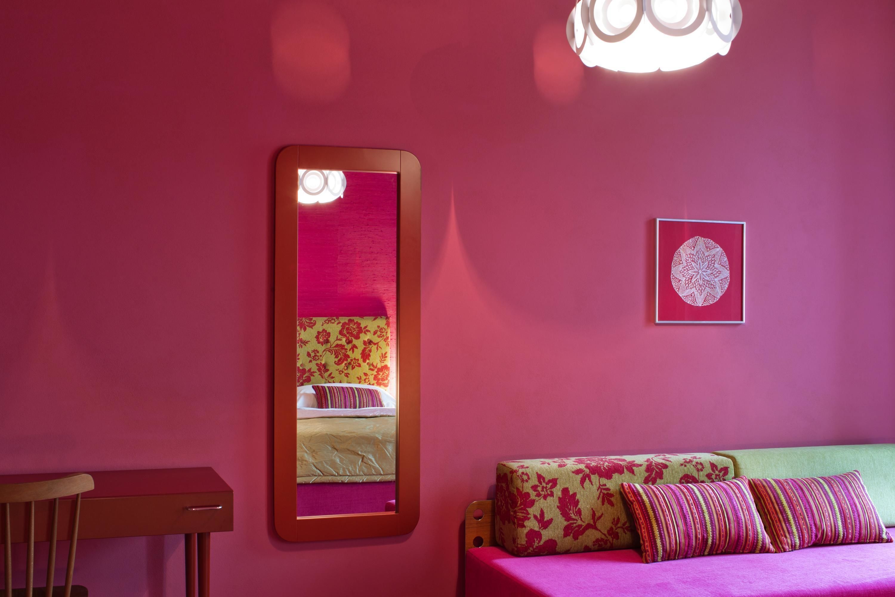 A room with a bed, a mirror, a small table, and a wall-mounted light fixture.