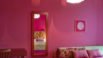 A room with a bed, a mirror, a small table, and a wall-mounted light fixture.