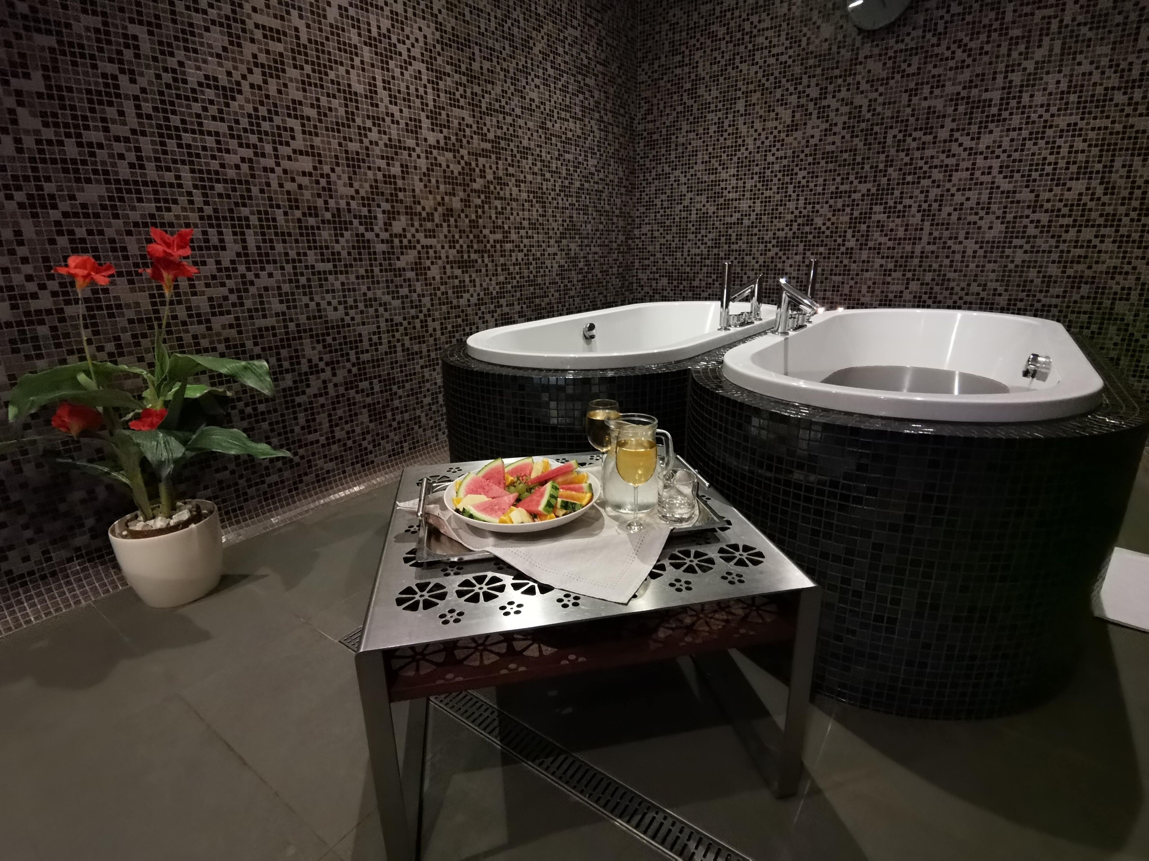 Ein Badezimmer mit zwei Waschbecken, einer Topfpflanze und einem Tisch mit Obstschale und Getränken.