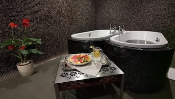 Ein Badezimmer mit zwei Waschbecken, einer Topfpflanze und einem Tisch mit Obstschale und Getränken.