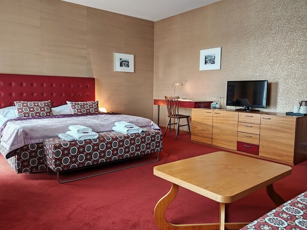 Una camera d'albergo con un letto, una scrivania, una TV e un tavolino.