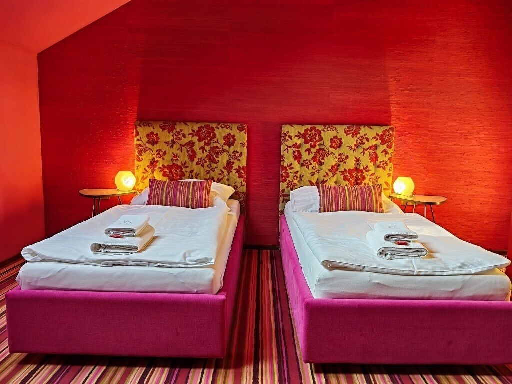 Two beds with pink headboards and floral-patterned headboards, each with a bedside lamp and neatly made beds.