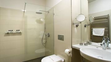 A modern bathroom with a glass-enclosed shower, a toilet, a sink with a mirror, and a towel rack.