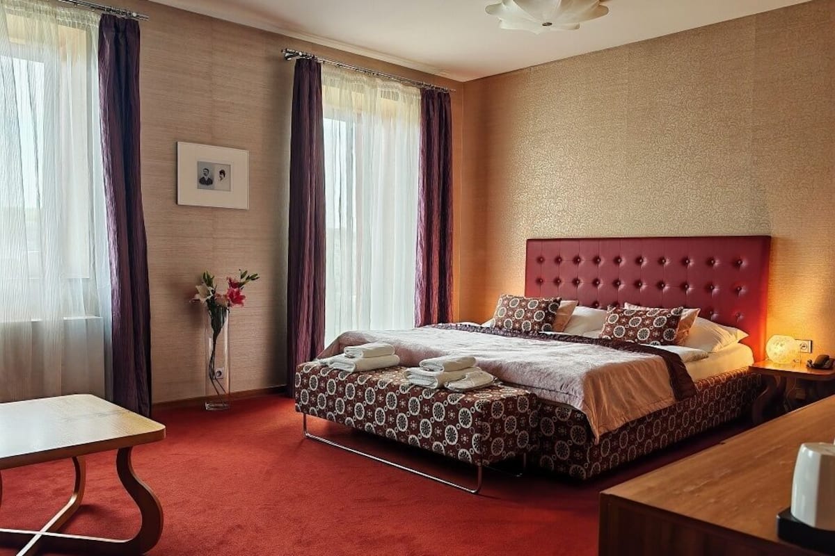 A hotel room with a large bed, a bedside table, a desk, and a chair.
