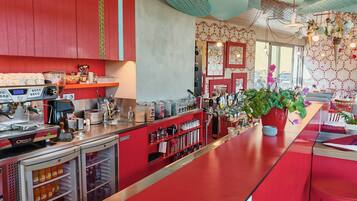 A bar area with a red counter, a coffee machine, and a refrigerator stocked with beverages.