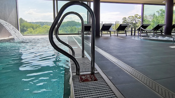 Una piscina interior con agua cristalina, un trampolín y sillas de descanso.