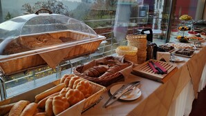 Un bufé con varios panes y pasteles, un cuchillo y un tenedor sobre un plato, y una vista de edificios al fondo.