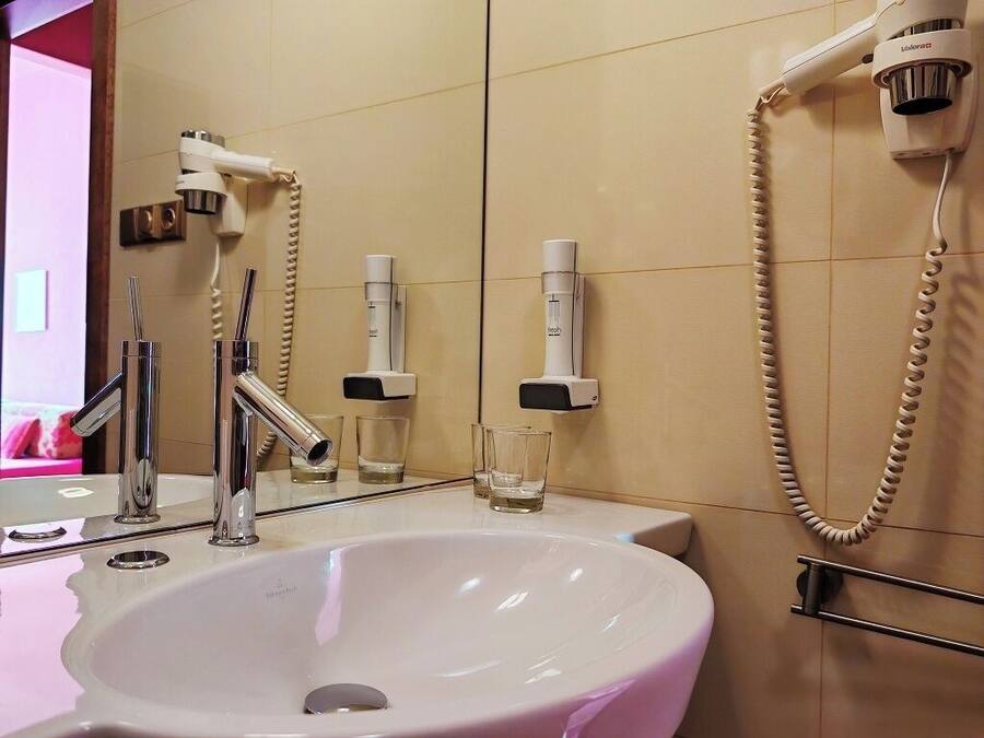 A bathroom with a white sink, chrome faucets, a handheld showerhead, and a mirror.
