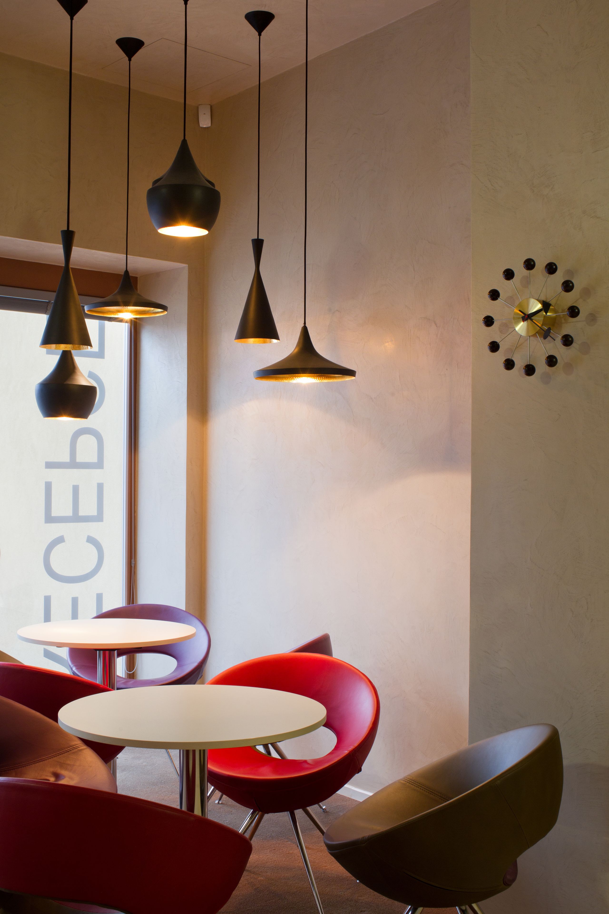A modern interior with pendant lighting, red chairs, and a round table.