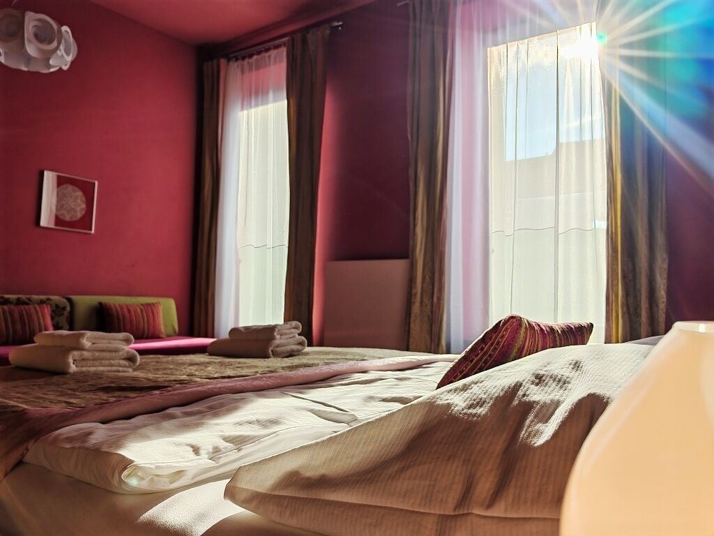 Ett hotellrum med en säng, kuddar, ett sängbord och gardiner.