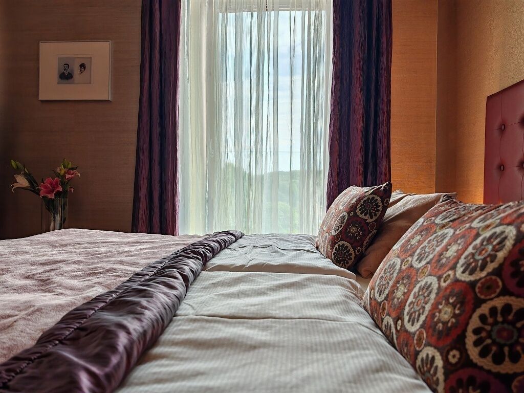 Una cama bien hecha con almohadas estampadas, un jarrón con flores y una foto enmarcada en la pared.