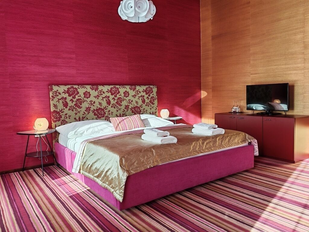 A hotel room with a large bed, a television, a small table with a lamp, and a wooden cabinet.