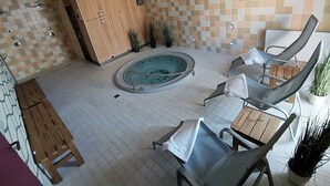Un área de spa con una bañera de hidromasaje, asientos de madera y paredes con azulejos.