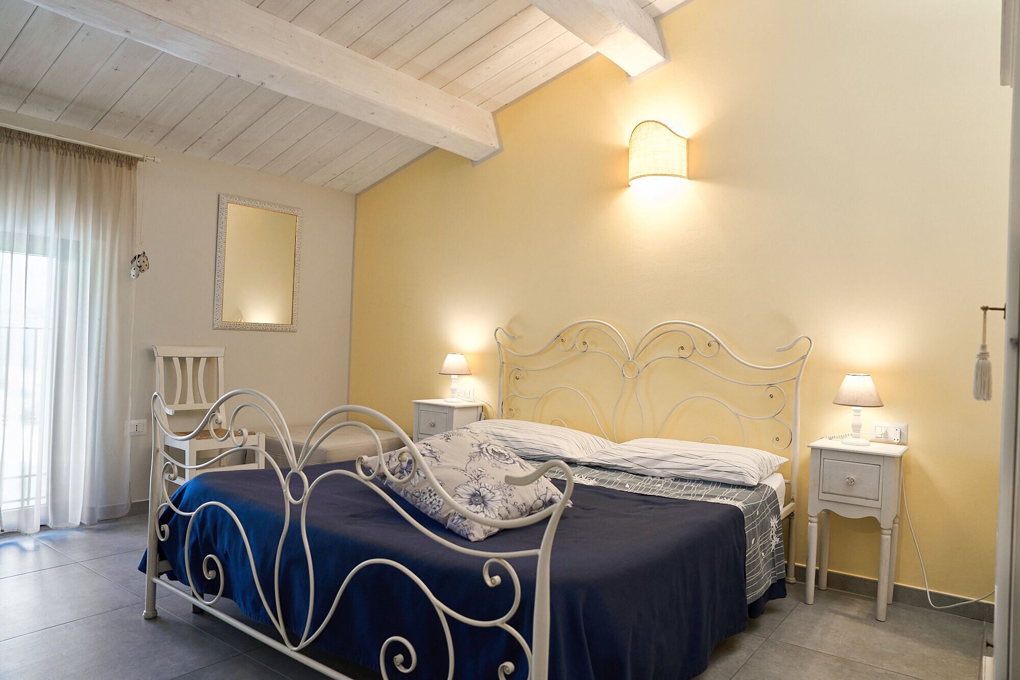 Une chambre à coucher avec un lit, des tables de chevet, un miroir et une lampe.