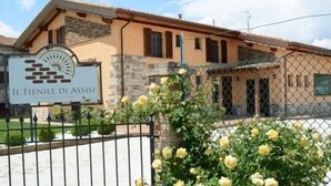 A building with a sign reading "Il Fienile Di Assisi," surrounded by a chain-link fence and yellow roses. - Il Fienile di Assisi (Assisi)