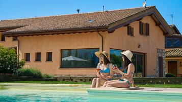 Two people sitting by a pool with a house in the background.