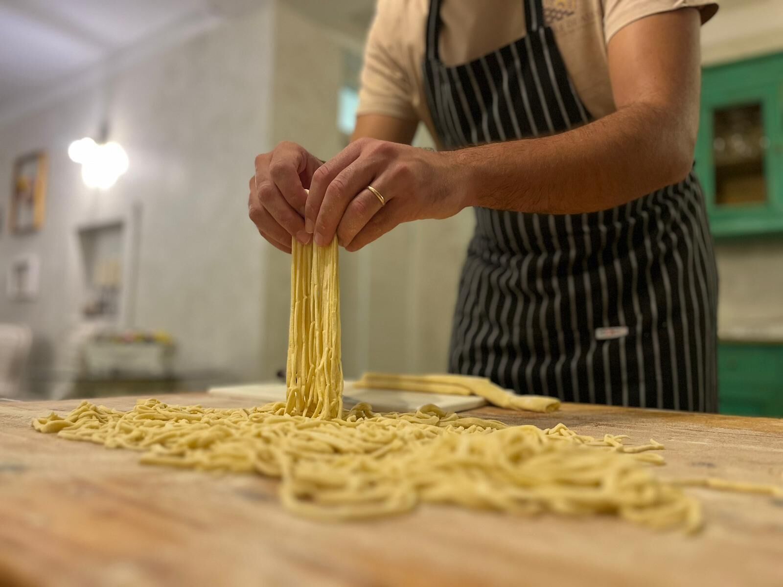 A person preparing pasta on a wooden table in a kitchen.