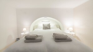 A neatly made bed with a pillow and two folded towels, a bedside table with a lamp, and a wall-mounted light fixture. - happy home Budapest JOY (Budapest)
