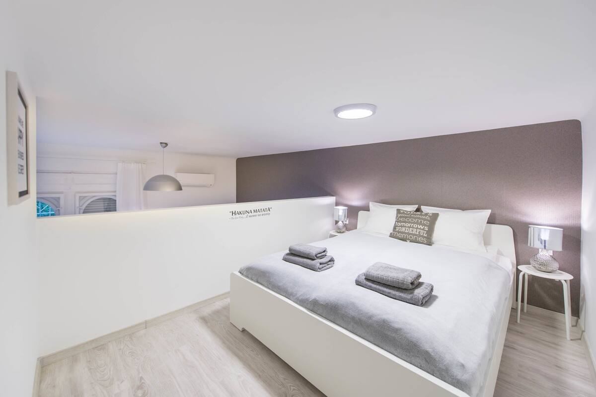 A modern bedroom with a bed, bedside tables, and a wall-mounted mirror.