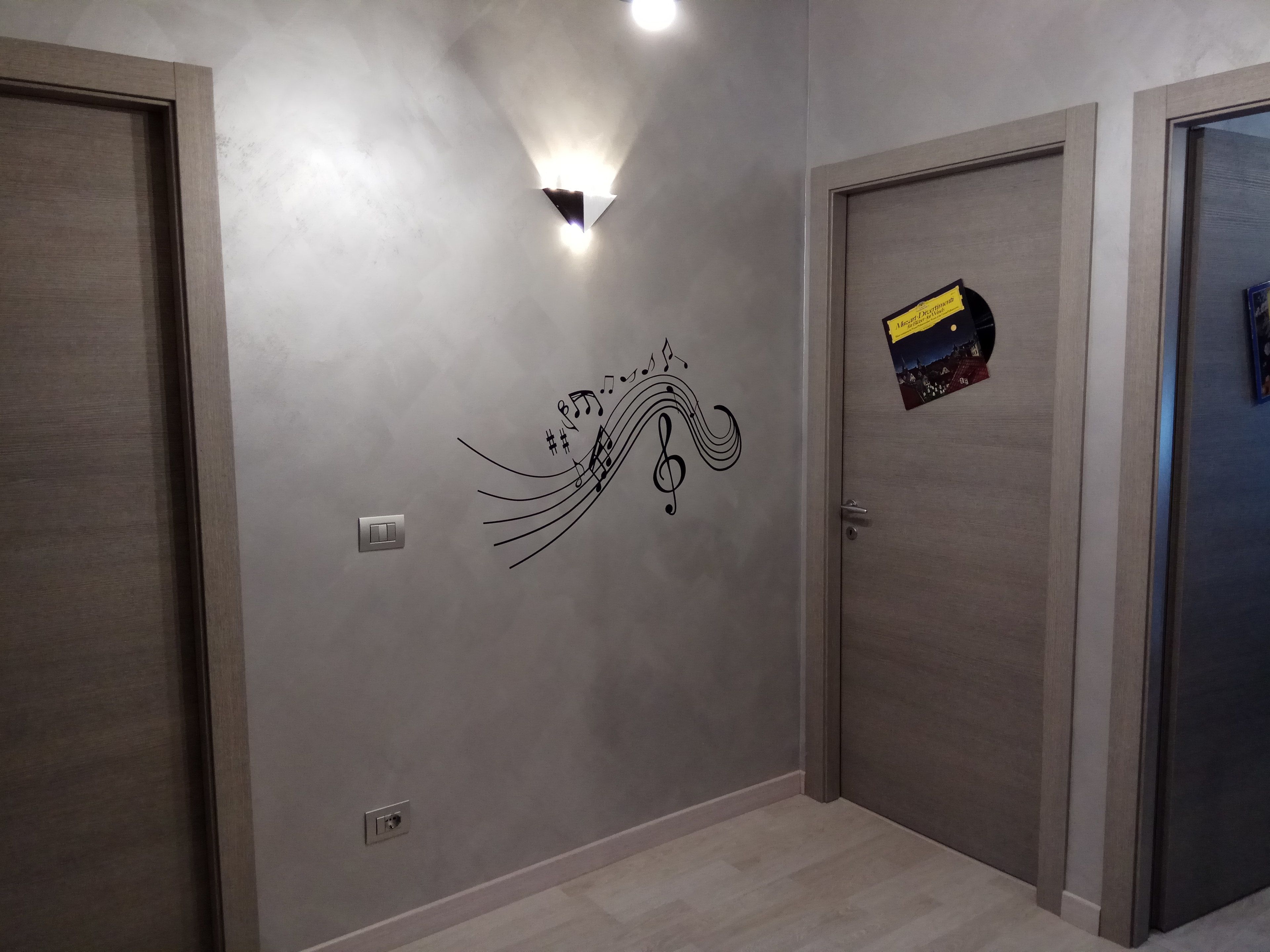 A hallway with grey walls, a decorative wall art of musical notes, and a door with a yellow and black sticker.