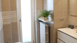 A modern bathroom with a toilet, bidet, sink, and a potted plant on a shelf. - B&B SanRock (Cuneo)