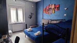 A bedroom with two beds, a window with curtains, a radiator, and a wall with artwork. - B&B SanRock (Cuneo)