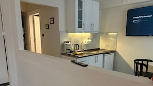 Una cocina moderna con armarios blancos, una cafetera y un televisor montado en la pared.