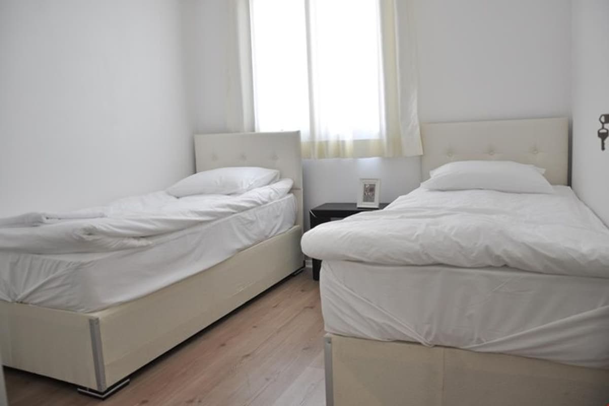 Two single beds with white bedding in a room with a wooden floor and a window with curtains.