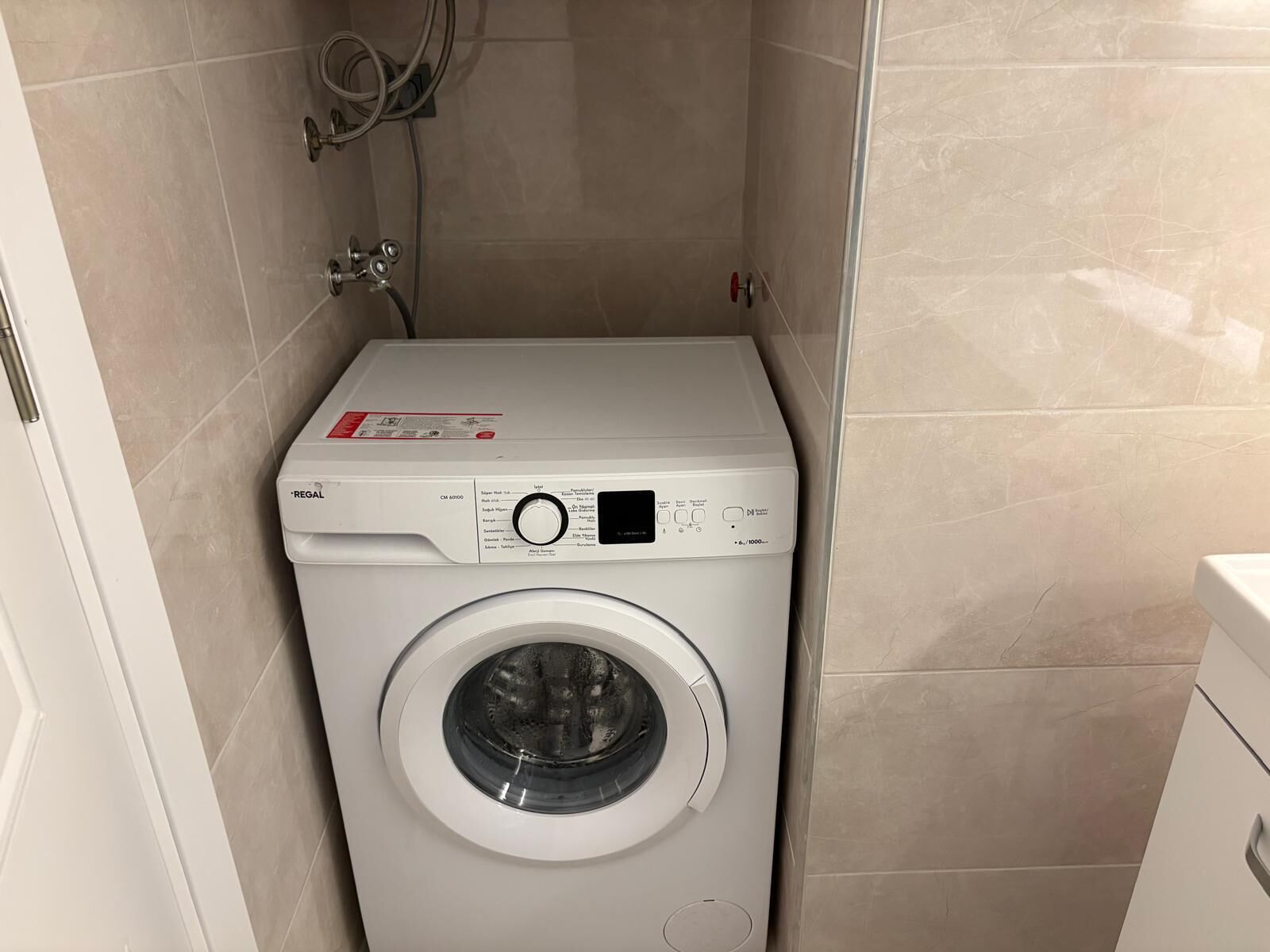 Lavadora compacta de carga frontal, blanca, en un baño pequeño con azulejos.