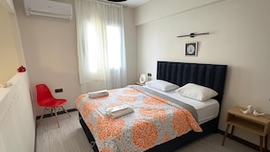 Un dormitorio con cama, una silla roja, una mesita de noche y una ventana con cortinas.