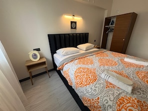 A hotel room with a bed, bedside table, nightstand, wardrobe, and a wall-mounted light fixture. - Deka Evleri (Izmir)