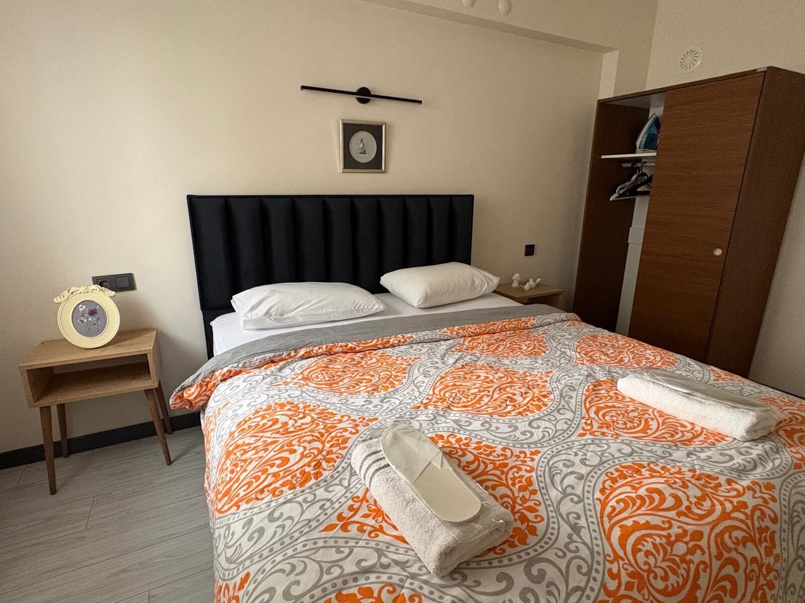 A hotel room with a bed, a nightstand, a wardrobe, and a framed picture on the wall.