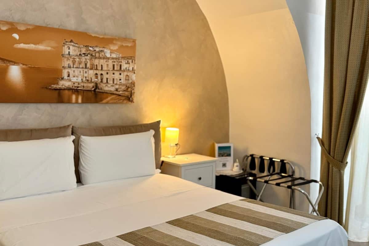 A hotel room with a large bed, a nightstand, a lamp, and a chair.