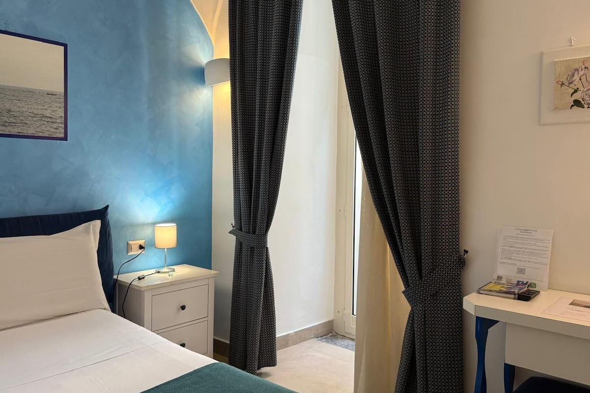 A hotel room with a bed, bedside table, lamp, and curtains.