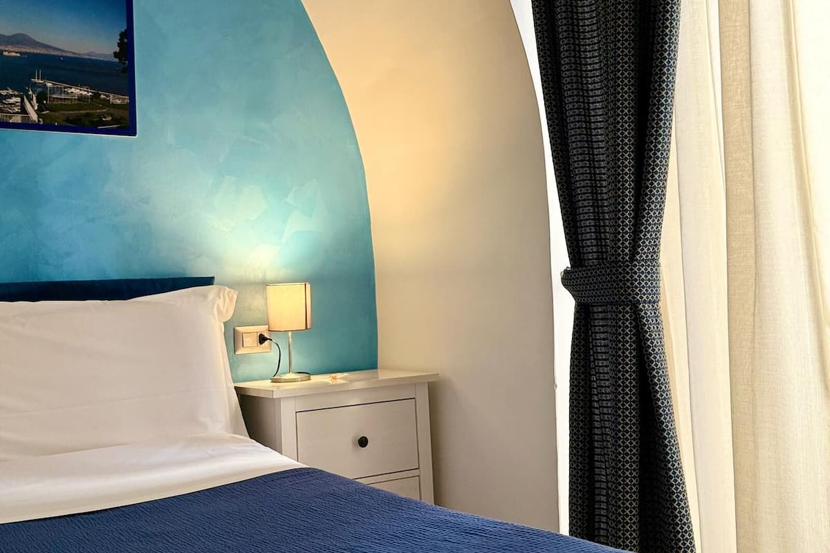 A hotel room with a bed, a nightstand, a lamp, and a view of the ocean.
